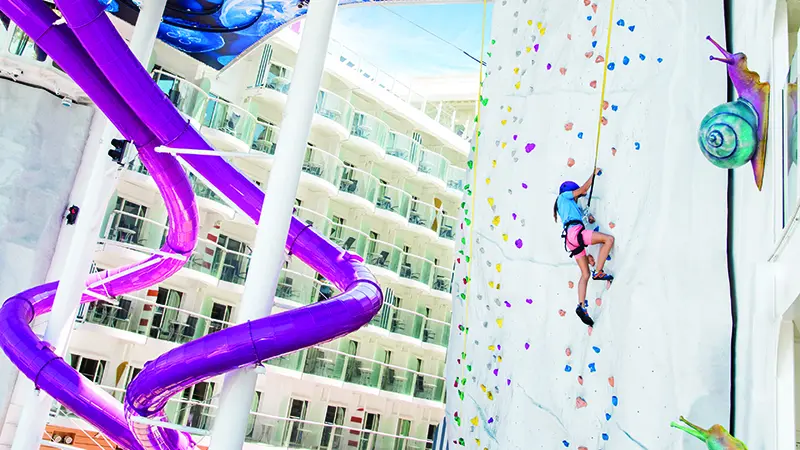 A young girl is climbing up the rock wall on the right with two long spiral purple slides on the left.